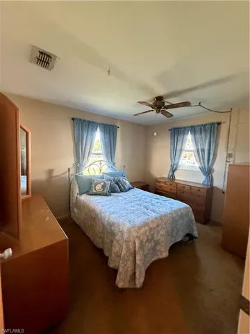 Bedroom featuring a ceiling fan, multiple windows, and dark carpet