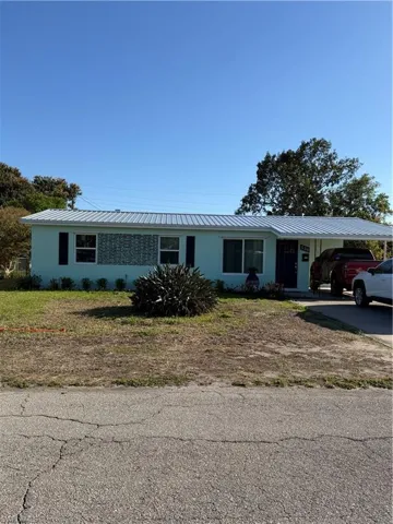 Ranch-style house with concrete driveway, an attached carport, a metal roof, and a front yard