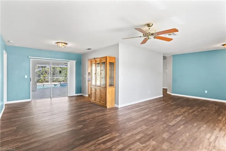 Unfurnished living room with a ceiling fan, visible vents, dark wood finished floors, and baseboards