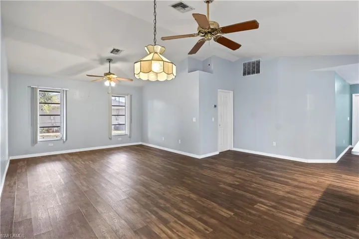 Spare room with dark wood-type flooring, visible vents, and baseboards