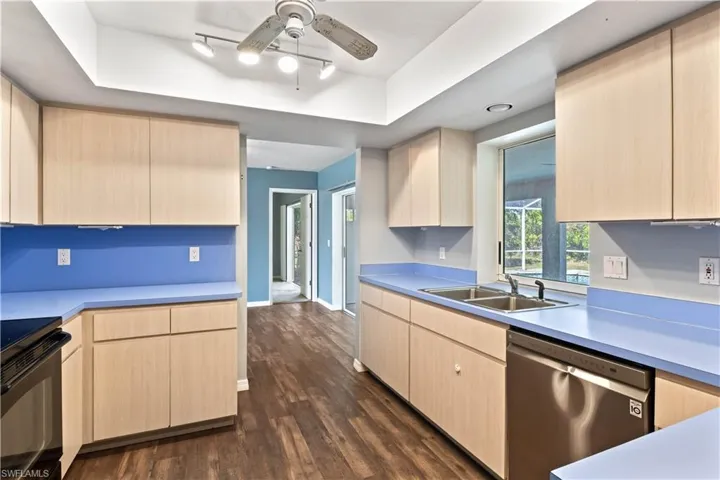 Kitchen with black / electric stove, a sink, dishwasher, light brown cabinetry, and a raised ceiling