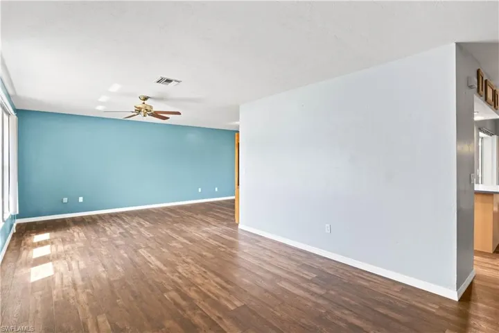 Unfurnished room with a ceiling fan, visible vents, baseboards, and wood finished floors