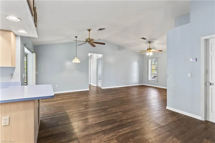 Unfurnished living room with dark wood finished floors, visible vents, a ceiling fan, vaulted ceiling, and baseboards