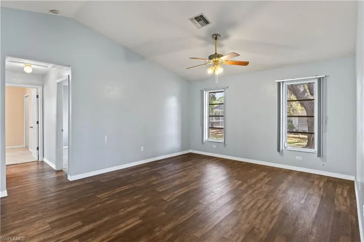 Empty room featuring baseboards, visible vents, a ceiling fan, lofted ceiling, and dark wood-type flooring