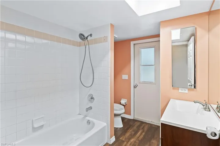Full bath with toilet, wood finished floors, vanity, baseboards, and shower / bathing tub combination