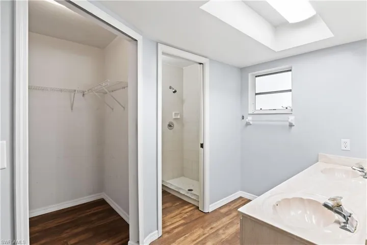 Full bath with a tile shower, a spacious closet, wood finished floors, and a sink