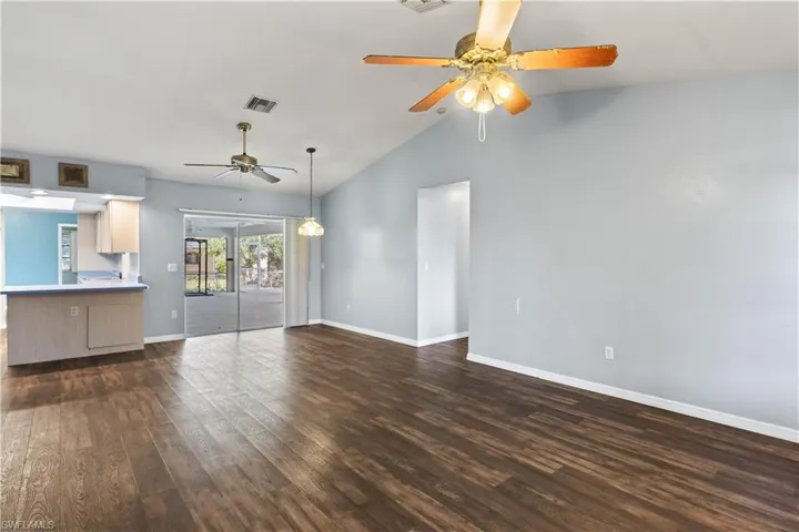 Unfurnished living room featuring ceiling fan, dark wood-style flooring, visible vents, baseboards, and vaulted ceiling