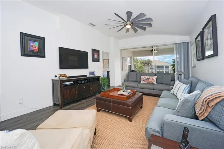 Living area with wood finished floors, lofted ceiling, baseboards, visible vents, and ceiling fan