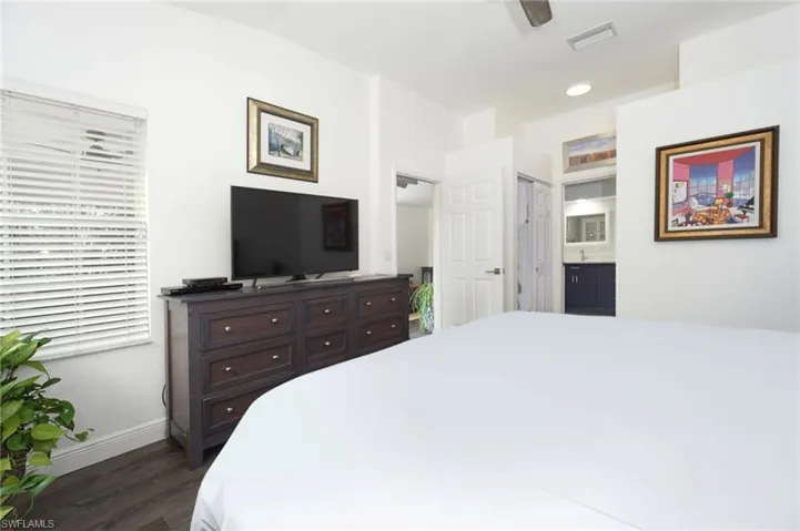 Bedroom with lofted ceiling, ensuite bath, baseboards, visible vents, and dark wood-type flooring