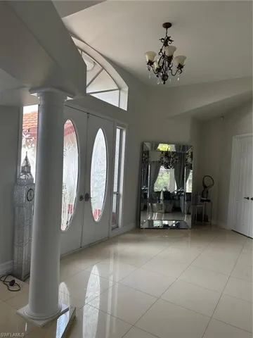 Tiled foyer entrance with decorative columns, an inviting chandelier, and baseboards