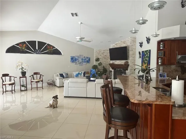 Living room with lofted ceiling, light tile patterned floors, visible vents, a ceiling fan, and a stone fireplace