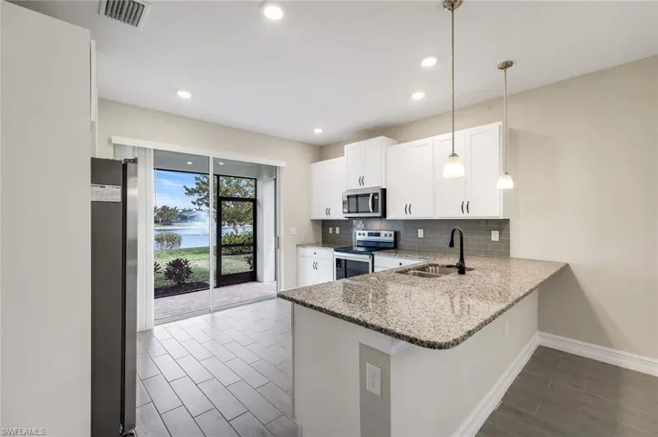 Kitchen featuring light stone counters, white cabinets, decorative light fixtures, appliances with stainless steel finishes, and backsplash
