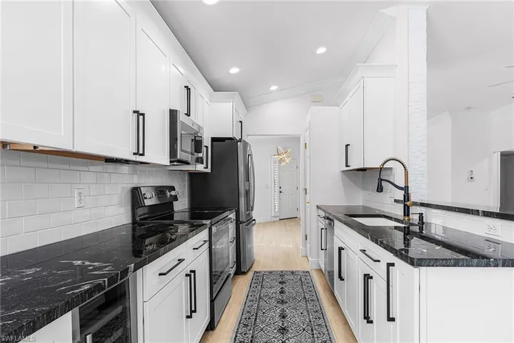 Kitchen featuring sub-way tile backsplash, stainless steel appliances, granite counters, light wood finished floors, and white cabinetry