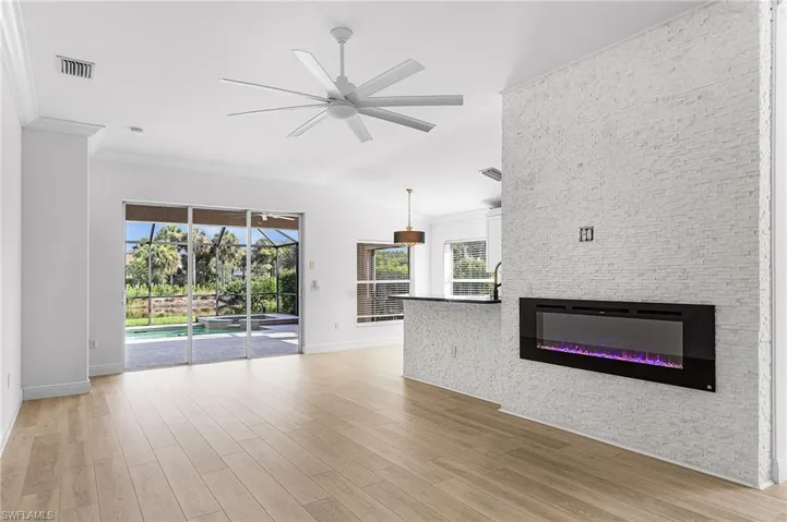 Spacious great room with crown molding, electric fireplace with stacked stone back drop, wood-like luxury vinyl floors, ceiling fan.