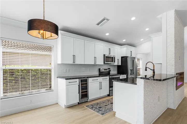 Kitchen with stainless steel appliances, granite countertops, white cabinets, decorative backsplash, and wine cooler