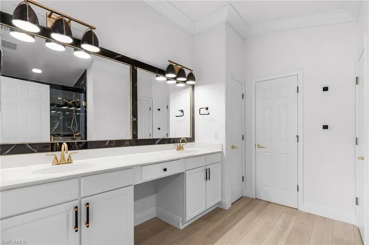 Owner's bath featuring double sinks, sit-down vanity, linen closet, wood finished LTV floors, and crown molding.
