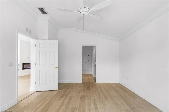 Primary bedroom with large walk-in closet, crown molding, light wood finished floors, vaulted ceiling, and ceiling fan.