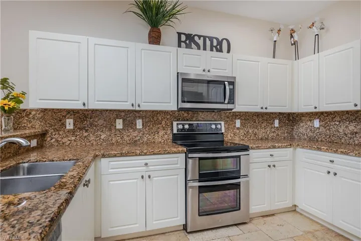 Kitchen with backsplash, sink, white cabinetry, and stainless steel appliances