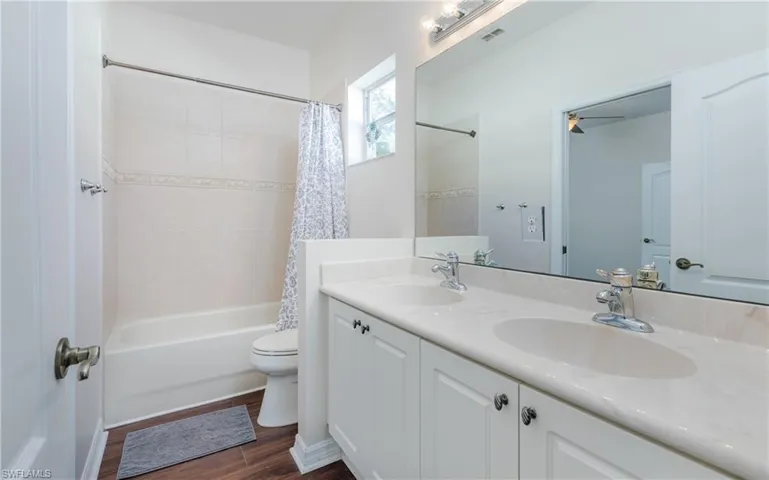 Full bathroom with wood-style floors, vanity, ceiling fan, toilet, and shower / tub combo
