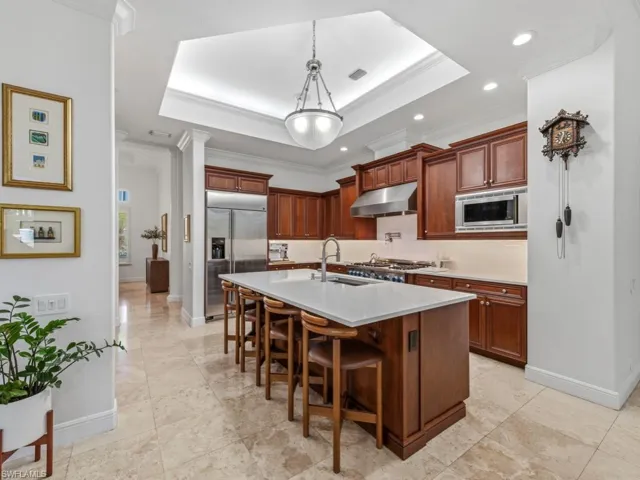 Kitchen with a kitchen breakfast bar, a tray ceiling, built in appliances, hanging light fixtures, and a center island with sink