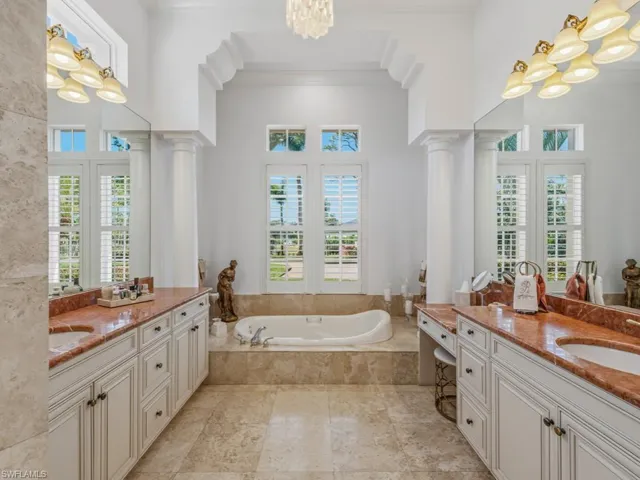 Full bath featuring a chandelier, a garden tub, two vanities, ornamental molding, and healthy amount of natural light
