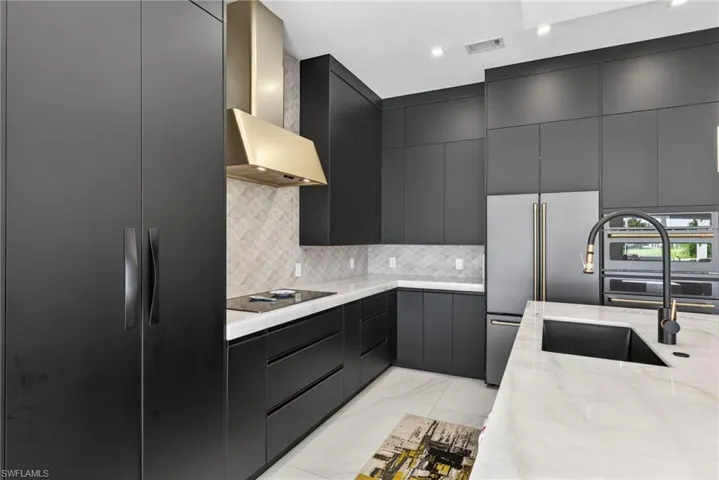 Kitchen with modern cabinets, wall chimney exhaust hood, light stone countertops, built in refrigerator, and tasteful backsplash