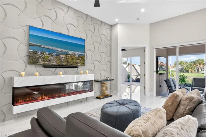 Living room featuring ceiling fan, a premium fireplace, an accent wall, recessed lighting, and light marble finish floors