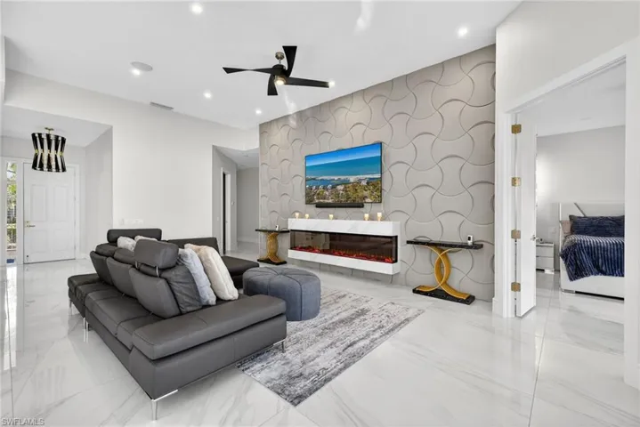 Living room featuring an accent wall, a ceiling fan, light marble finish flooring, recessed lighting, and a glass covered fireplace