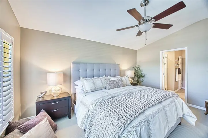 Carpeted bedroom with vaulted ceiling, a ceiling fan, and connected bathroom