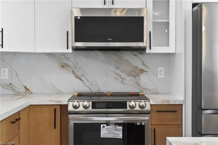 Kitchen with stainless steel appliances, light stone counters, glass insert cabinets, wood finish cabinetry, and tasteful backsplash