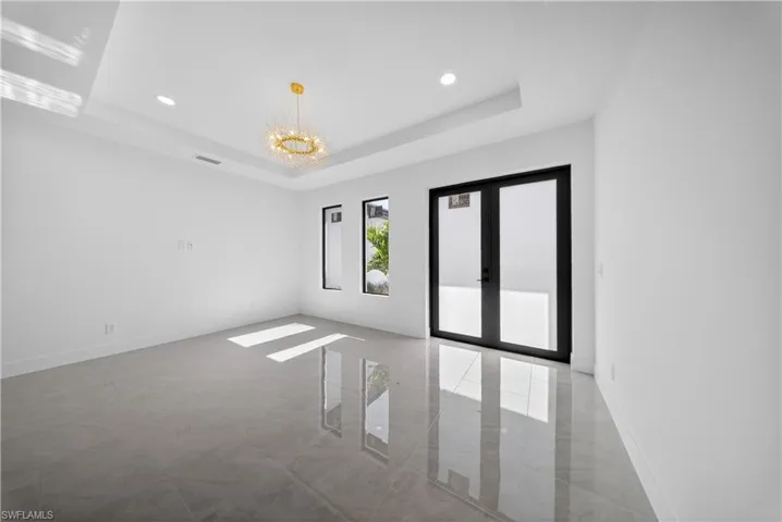 Empty room with french doors, suspended lighting, and a tray ceiling