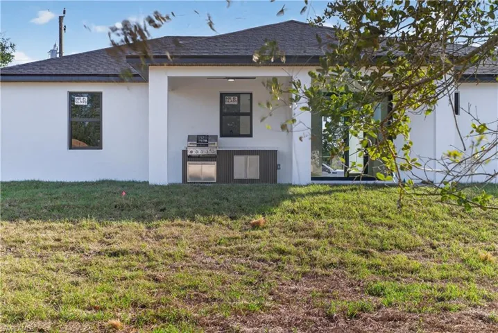 Back of property featuring stucco siding, roof with shingles, a yard, and covered porch