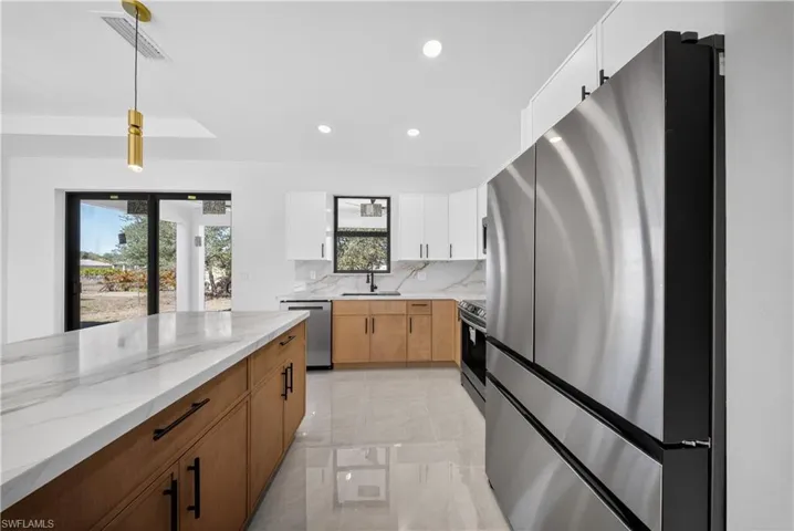 Kitchen with stainless steel appliances, dual tone cabinetry, hanging light fixtures, light stone countertops, and tasteful backsplash