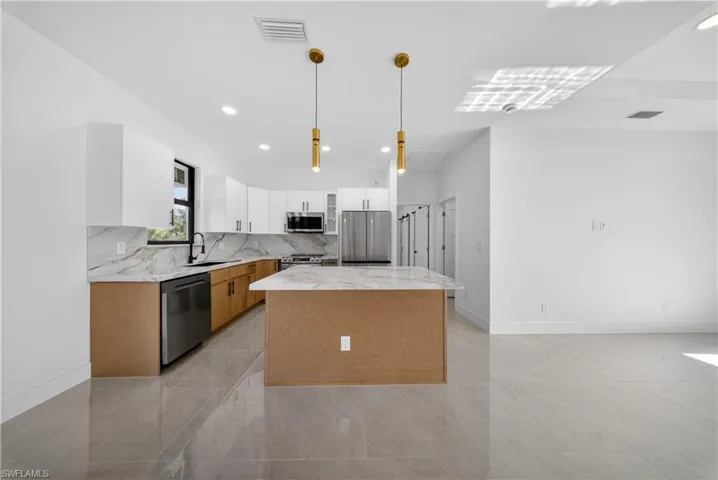Kitchen with two tone cabinets, a center island, light stone countertops, decorative light fixtures, and stainless steel appliances