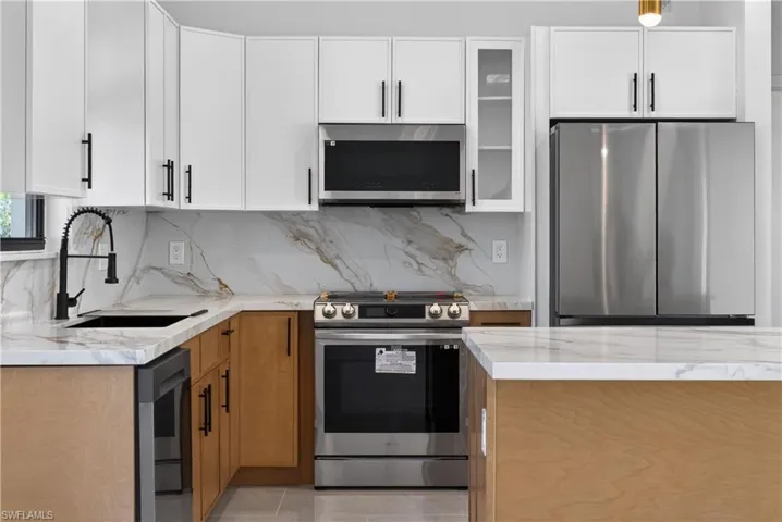 Kitchen featuring stainless steel appliances, light stone countertops, glass insert cabinets, backsplash, and dual tone cabinetry