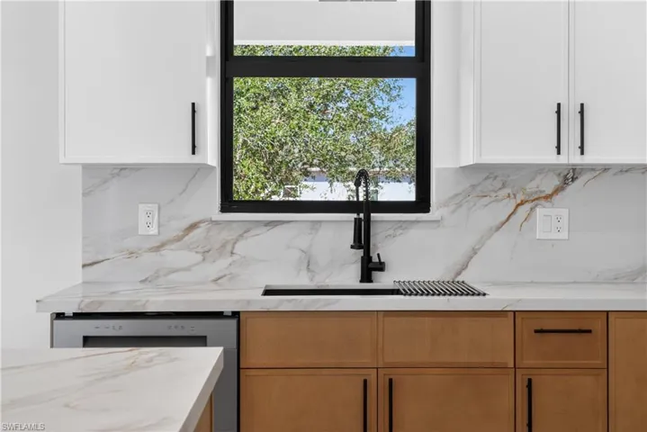 Kitchen with light stone counters, dishwasher, and white cabinets