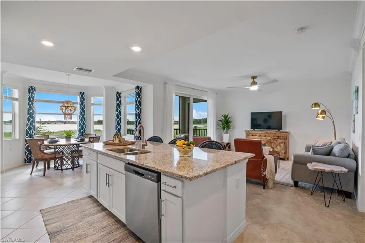 Kitchen featuring stainless steel dishwasher, light tile patterned flooring, white cabinetry, ceiling fan, and a kitchen island with sink