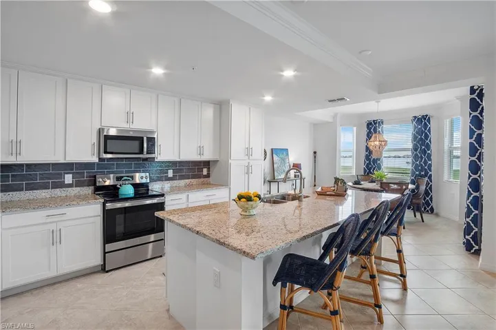 Kitchen with tasteful backsplash, white cabinets, ornamental molding, a center island with sink, and appliances with stainless steel finishes