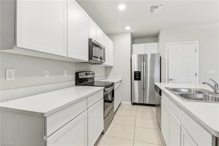 Kitchen featuring stainless steel appliances, white cabinetry, recessed lighting, light tile patterned flooring, and a kitchen island with sink