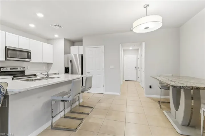 Kitchen with a kitchen breakfast bar, stainless steel appliances, hanging light fixtures, white cabinets, and recessed lighting