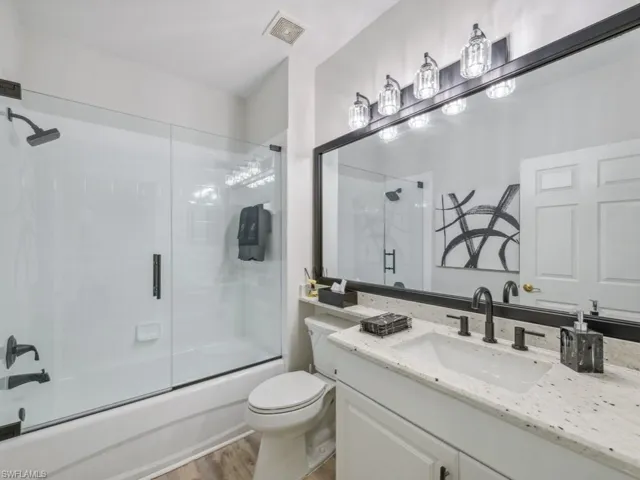 Bathroom with toilet, vanity, wood finished floors, visible vents, and shower / bath combination with glass door
