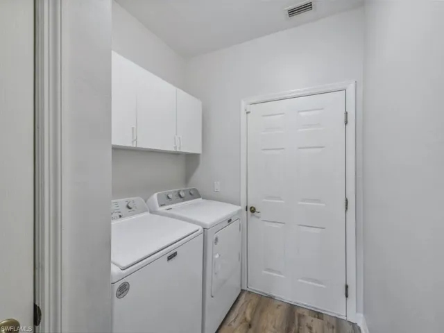 Washroom featuring visible vents, wood finished floors, washing machine and dryer, and cabinet space