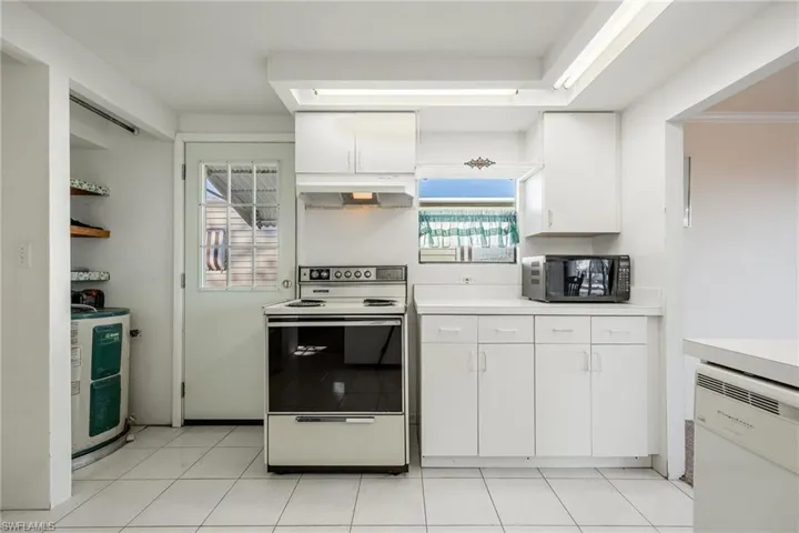 Kitchen featuring water heater, white appliances, white cabinetry, light countertops, and under cabinet range hood
