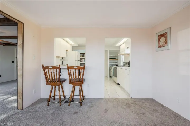 Kitchen with light carpet, a breakfast bar area, white appliances, and white cabinets