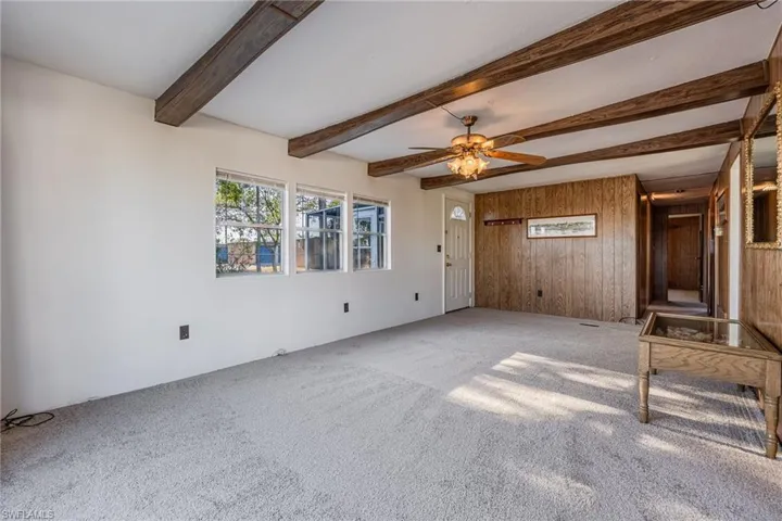 Unfurnished living room with wooden walls, a ceiling fan, beam ceiling, and new carpet