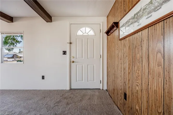 Foyer featuring wooden walls, beam ceiling, and new carpet flooring