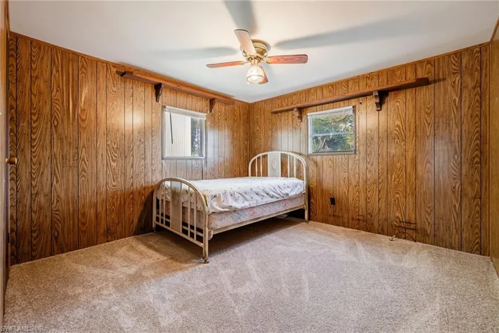 NEW Carpeted bedroom featuring wooden walls, multiple windows, and ceiling fan