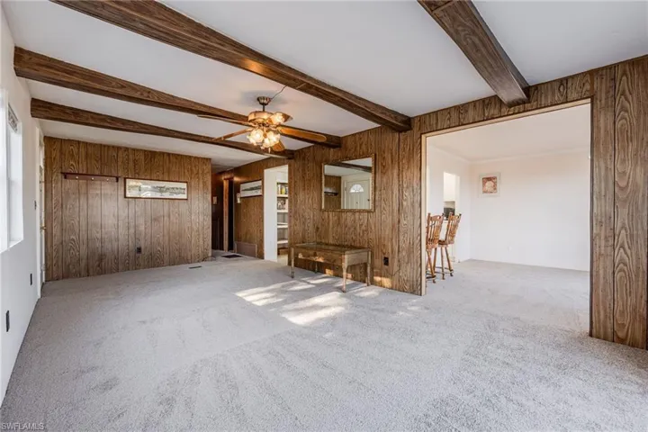 Carpeted living room featuring wooden walls, ceiling fan and a beam ceiling