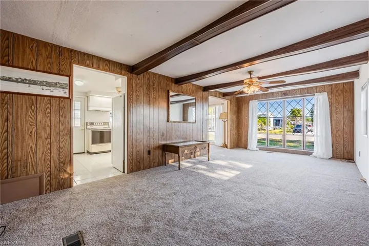 NEW Carpeted living room featuring wooden walls, beam ceiling and a ceiling fan