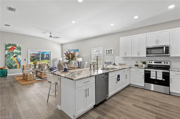 Kitchen with stainless steel appliances, white cabinetry, a peninsula, a kitchen breakfast bar, and vaulted ceiling